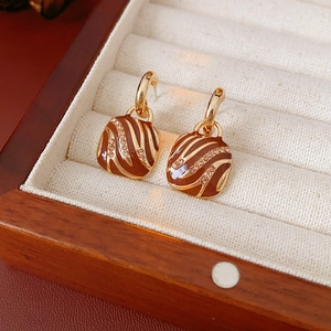Close-up of brown enamel earrings with gold trim and rhinestones on a jewelry box