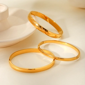 Close-up of three polished gold stainless steel bangles in wide and narrow sleek designs