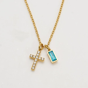Macro shot of gold cross necklace with clear zircons and blue rectangular gemstone pendant