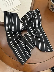 Detailed view of black and white striped satin scrunchie on a vintage wooden surface