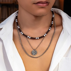 Men's layered necklace featuring brown wood beads and silver coin pendant on white shirt