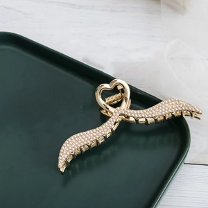 Elegant gold metal angel wing hair claw clip with white pearls on a green plate