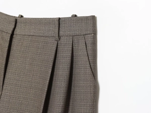 Detail of high-waisted trousers featuring double pleats and side pockets in brown tweed fabric