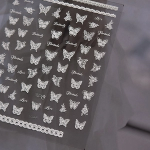 Macro shot of 3D embossed nail stickers featuring white lace butterflies and flower patterns
