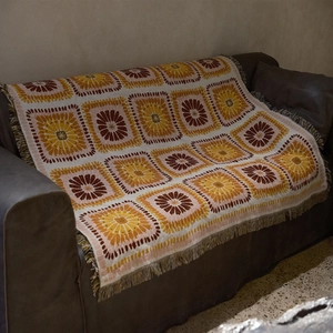 Retro bohemian knitted picnic blanket with sunflower patterns and tassel edges on leather sofa