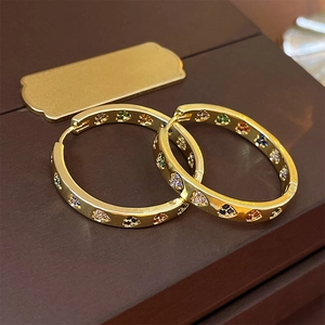 Detailed view of gold hoop earrings with heart patterns and colorful zircons on wood
