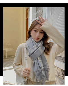 Gray plaid cashmere-like scarf detail showing soft texture and tassel on a model