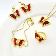 Detail of gold jewelry set with red butterfly necklace, bracelet and ring on white plate