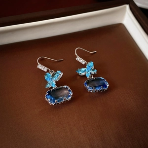 Detail of silver drop earrings featuring a blue crystal butterfly and large blue main stone