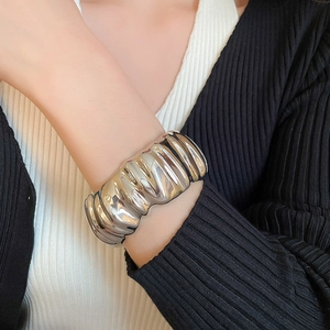 Détail d'un large bracelet manchette argenté avec design froissé texturé porté au poignet
