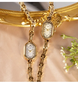 Detail view of two gold quartz watches with chain bands and oval dials on silk fabric