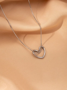 Macro shot of a silver heart pendant on a snake chain over champagne silk fabric