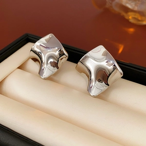 Détail macro de boucles d'oreilles carrées argentées irrégulières sur un écrin de bijoux