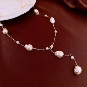 Detail of baroque pearl necklace with gold-plated Y-chain on dark velvet background