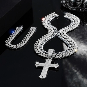 Silver iced-out Cuban chain necklace and bracelet set with cross pendant on black surface