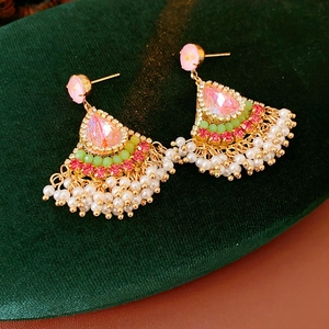 Dettaglio di orecchini vintage dorati con pietre rosa, perline verdi e frange di perle