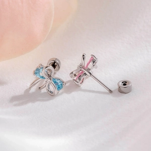 Silver ribbon bow earrings with blue and pink gems displayed on white petals