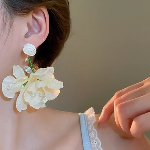 Close-up of model wearing white fabric flower tassel earrings with green beads