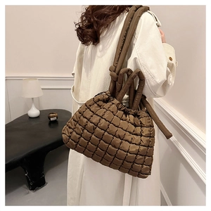 Detail of a brown quilted puffer tote bag with stylish knot handles on a model