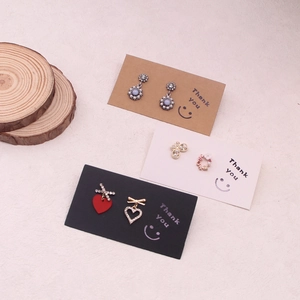 Various stud earrings displayed on Kraft paper cards with wood and texture background