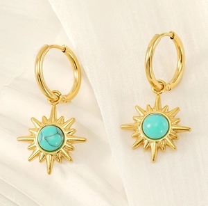 Close-up of golden sunburst drop earrings with turquoise center on textured fabric