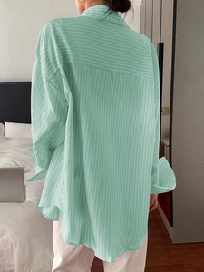 Detail of light green striped shirt showing relaxed fit and folded cuffs on the sleeves
