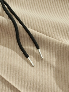 Macro shot of beige ribbed knit fabric with black woven drawstrings and silver metal tips