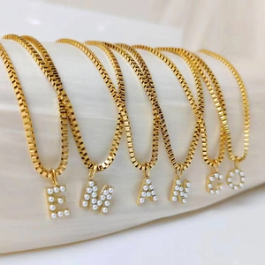 Detalle de collares de cadena dorada con colgantes de letras de perlas blancas E M A N C O