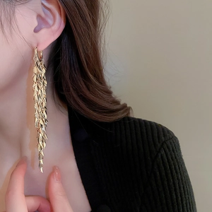 Close-up of elegant gold leaf tassel earrings worn by a model in a warm-toned setting