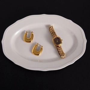 Ensemble boucles d'oreilles U dorées et montre rectangulaire sur plateau blanc