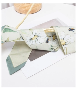 Close-up of narrow green daisy print silk scarf tied on a natural wooden stand