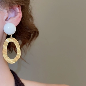 Close-up of model wearing brushed gold oval earrings with white resin beads