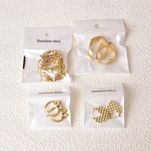 Detail showing four gold stainless steel earrings with heart, bow, and geometric patterns