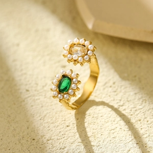Detail of gold open ring with green and clear gemstones and pearls on textured surface