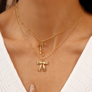Gros plan détaillé d'un collier doré à double épaisseur avec élégants pendentifs nœuds