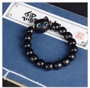 Détail d'un bracelet en perles de bois chat avec yeux bleus posé sur un livre ancien