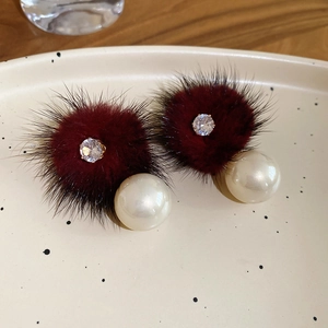 Close-up of burgundy plush earrings with zircon and white pearls on a ceramic dish