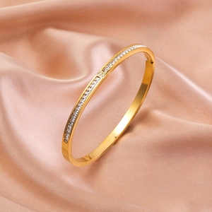 Elegante bracciale rigido in acciaio dorato con zirconi brillanti su sfondo di seta