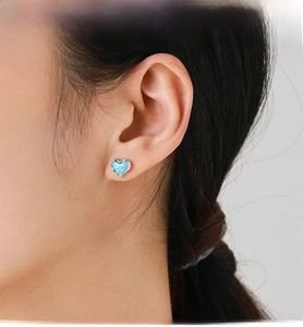 Close-up of a model wearing heart-shaped blue opal stud earrings in 925 silver