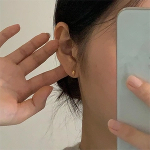 Minimalist gold oval stud earrings shown on earlobe in a mirror selfie perspective