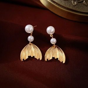 Detailed view of golden fishtail pendant earrings with white pearls on a dark red background