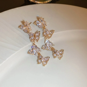 Macro detail of gold butterfly tassel earrings with sparkling cubic zirconia on a ceramic tray