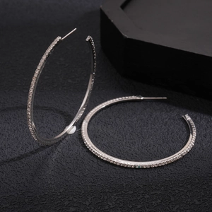 Close-up of silver geometric hoop earrings with sparkling rhinestones on black background