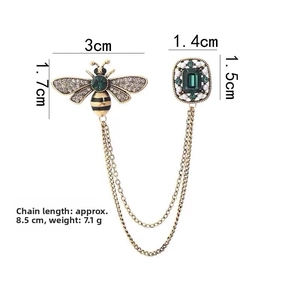 Detail of vintage bee brooch with green gemstone, golden chains and pearl embellishments