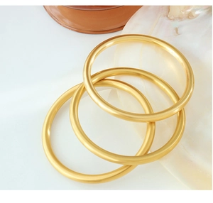 Detailed macro view of three matte gold geometric round bangles on a minimalist display