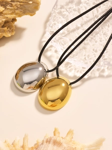 Close-up of minimalist gold and silver oval pendants with polished finish on black cord