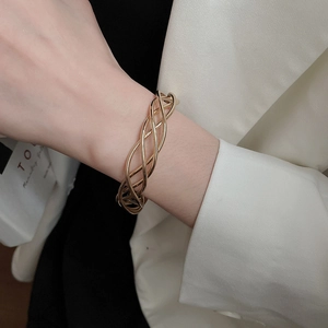 Detail of twisted gold metal cuff bracelet paired with a white elegant blazer
