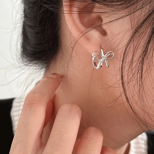 Close-up of a silver hollow bow earring worn on a model's ear with high metal luster