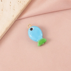 Macro shot of blue and green glass fish pendant with golden ring on pink fabric background