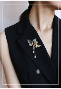 Détail de la broche papillon en zircon avec pompon doré sur un revers de blazer noir